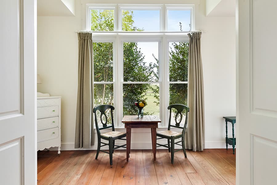 Cozy dining nook with two chairs and a table, framed by curtains and large windows overlooking greenery.