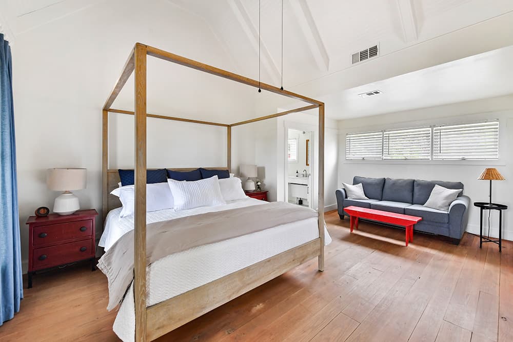 Bright bedroom with a four-poster bed, cozy seating area, and light wood flooring.