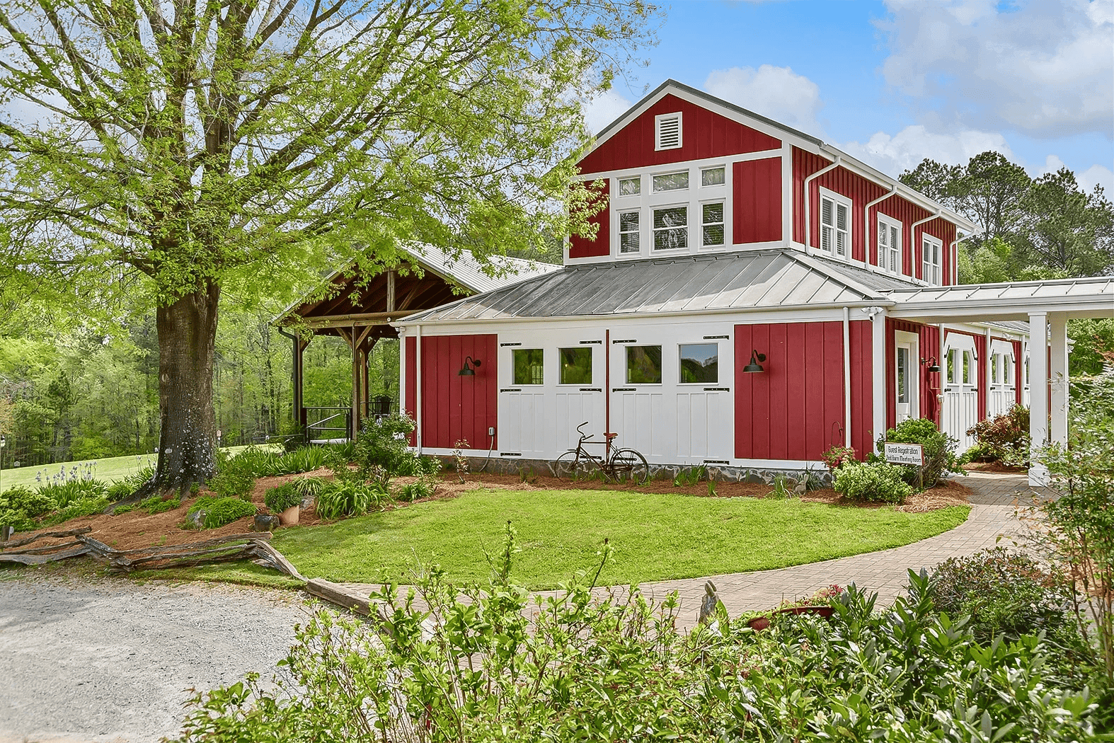 A red barn-style house with a covered porch, surrounded by green grass and trees on a sunny day.
