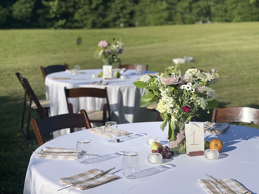 A beautifully set outdoor dining table with floral centerpieces and elegant place settings under a clear blue sky.
