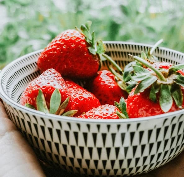 A bowl of fresh strawberries with green leaves.