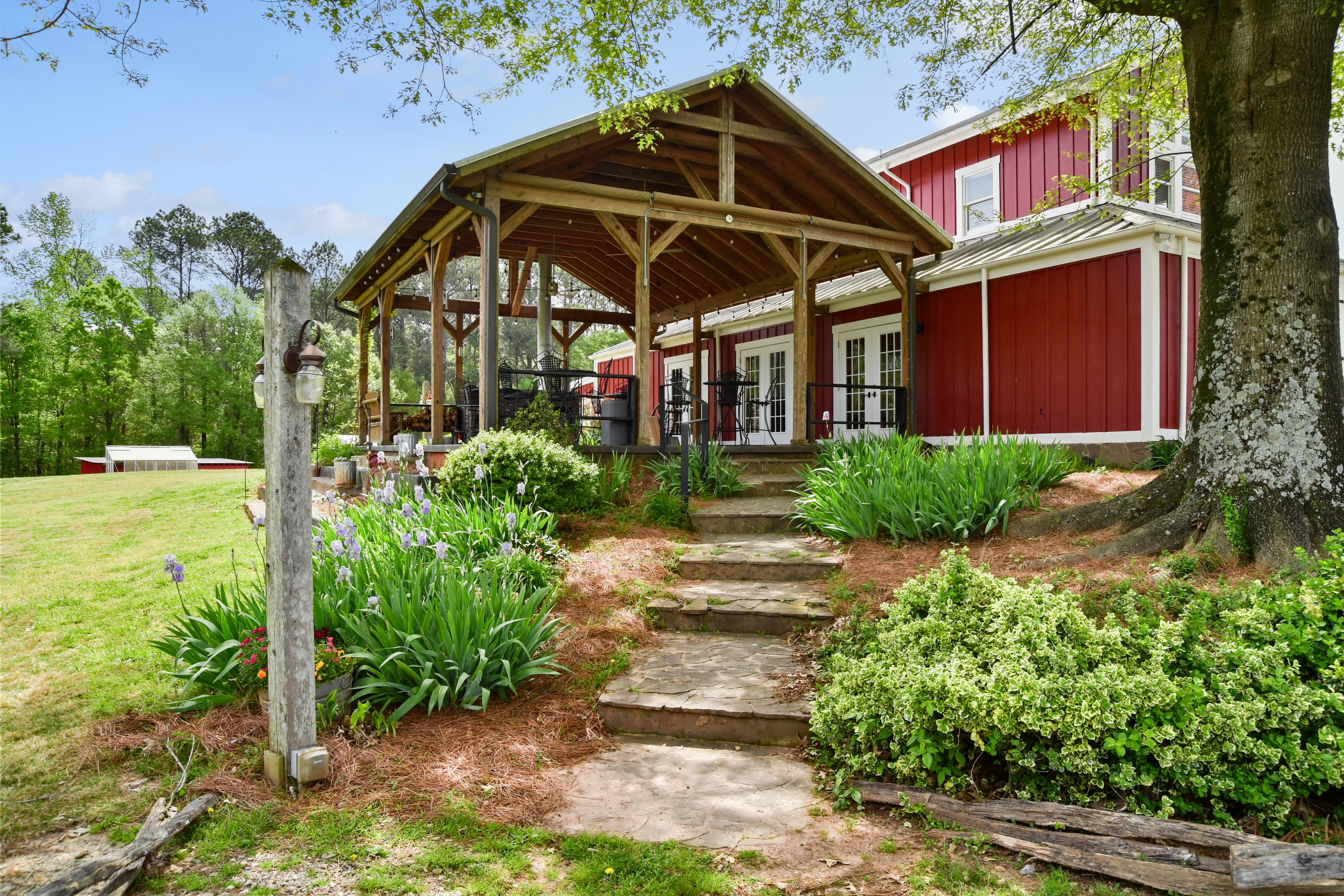A charming red barn-style building with a covered porch, surrounded by lush greenery and decorative flowers.