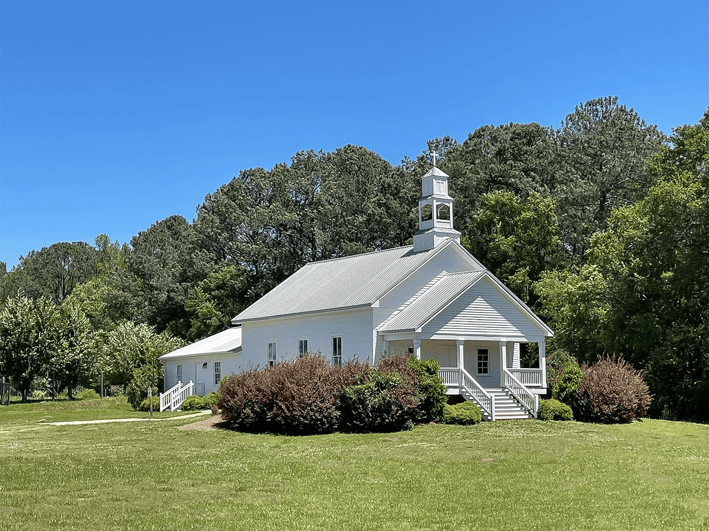 A white church building surrounded by greenery under a clear blue sky.